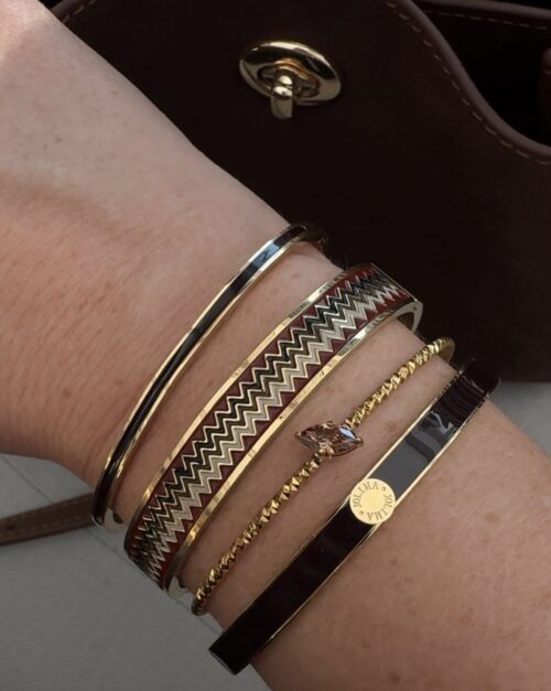 Närbild på en handled som bär fem armband, bland annat Armband Poppy i vinröd/guld och Antibes från By Jolima.