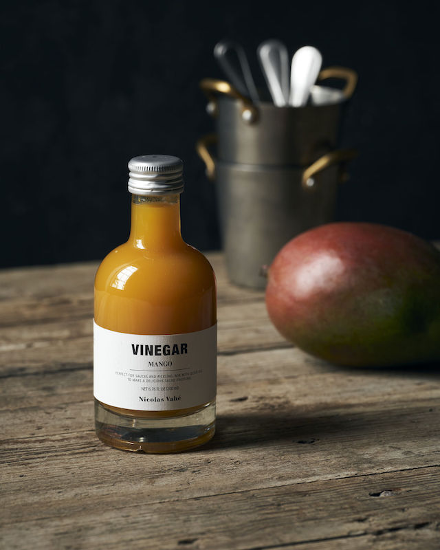 Vinäger med smak av Mango från Nicolas Vahé bredvid en mango och bestickkorg