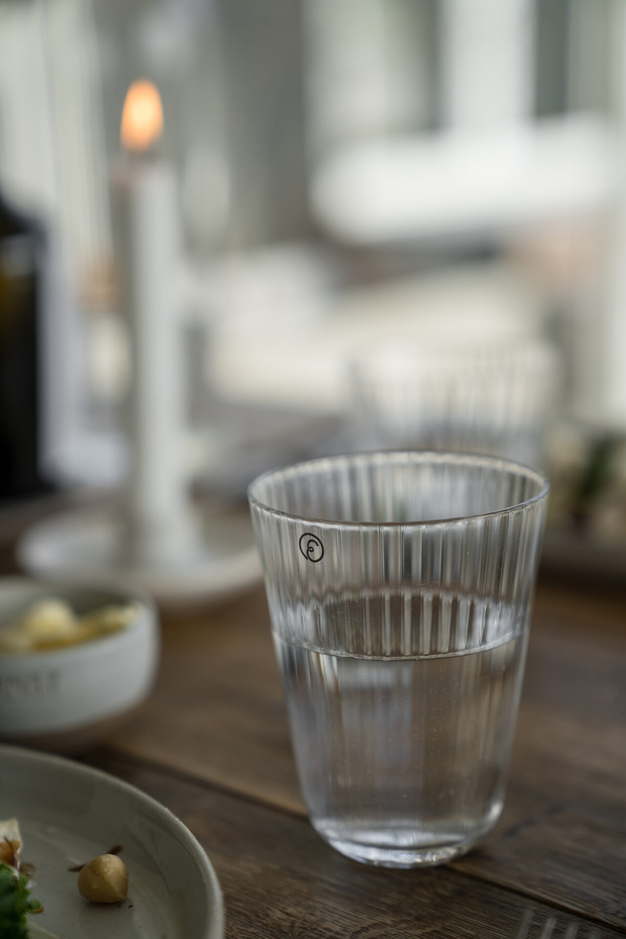 Räfflat dricksglas med vatten på dukat bord.