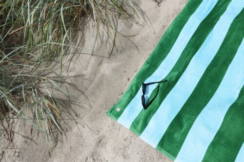 Randig handduk i färgsprakande blå/grön färger liggandes på stranden.
