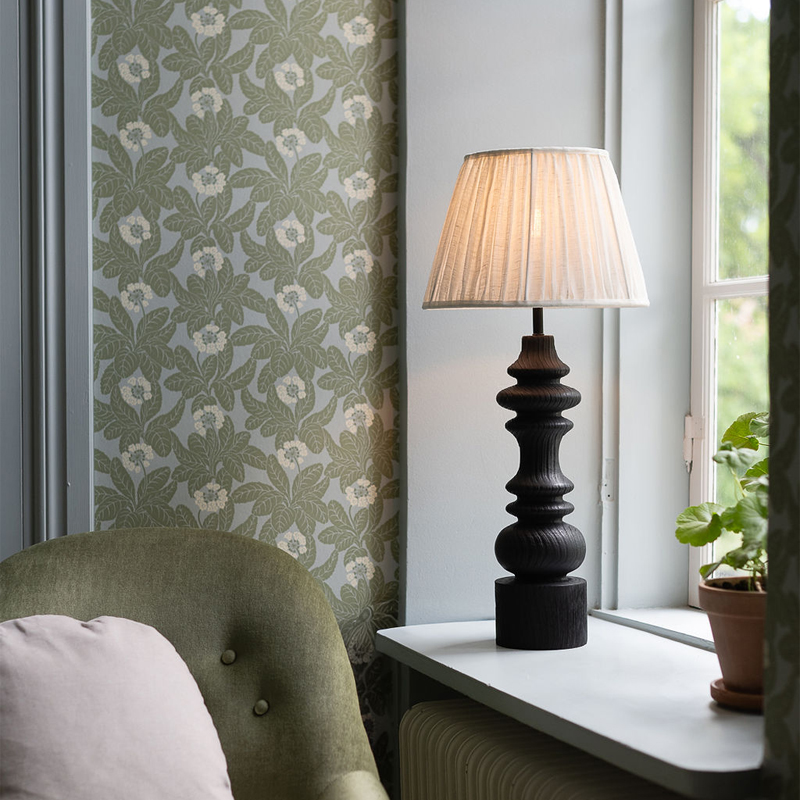 Lampfot Saga i svart trä med offwhite skärm står i ett fönster i ett rum i gröna toner.